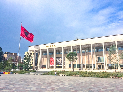 red flag with large opera house behind in tirana albania