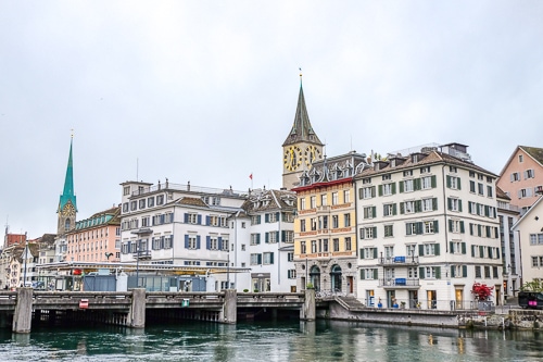 large clock tower with old town buildings and river in front in zurich switzerland