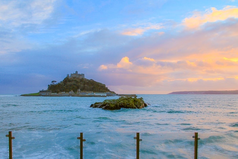blue shoreline with sun setting over st michaels mount in cornwall