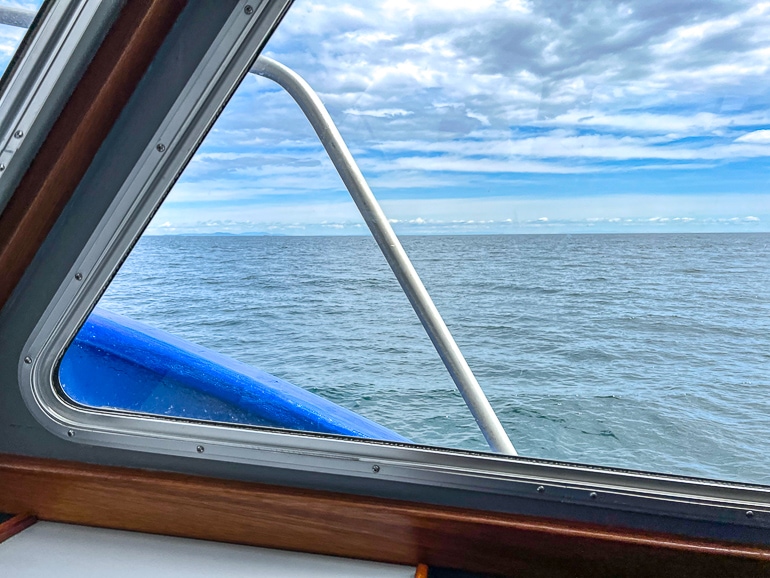 peering through glass window on boat looking out at open ocean.